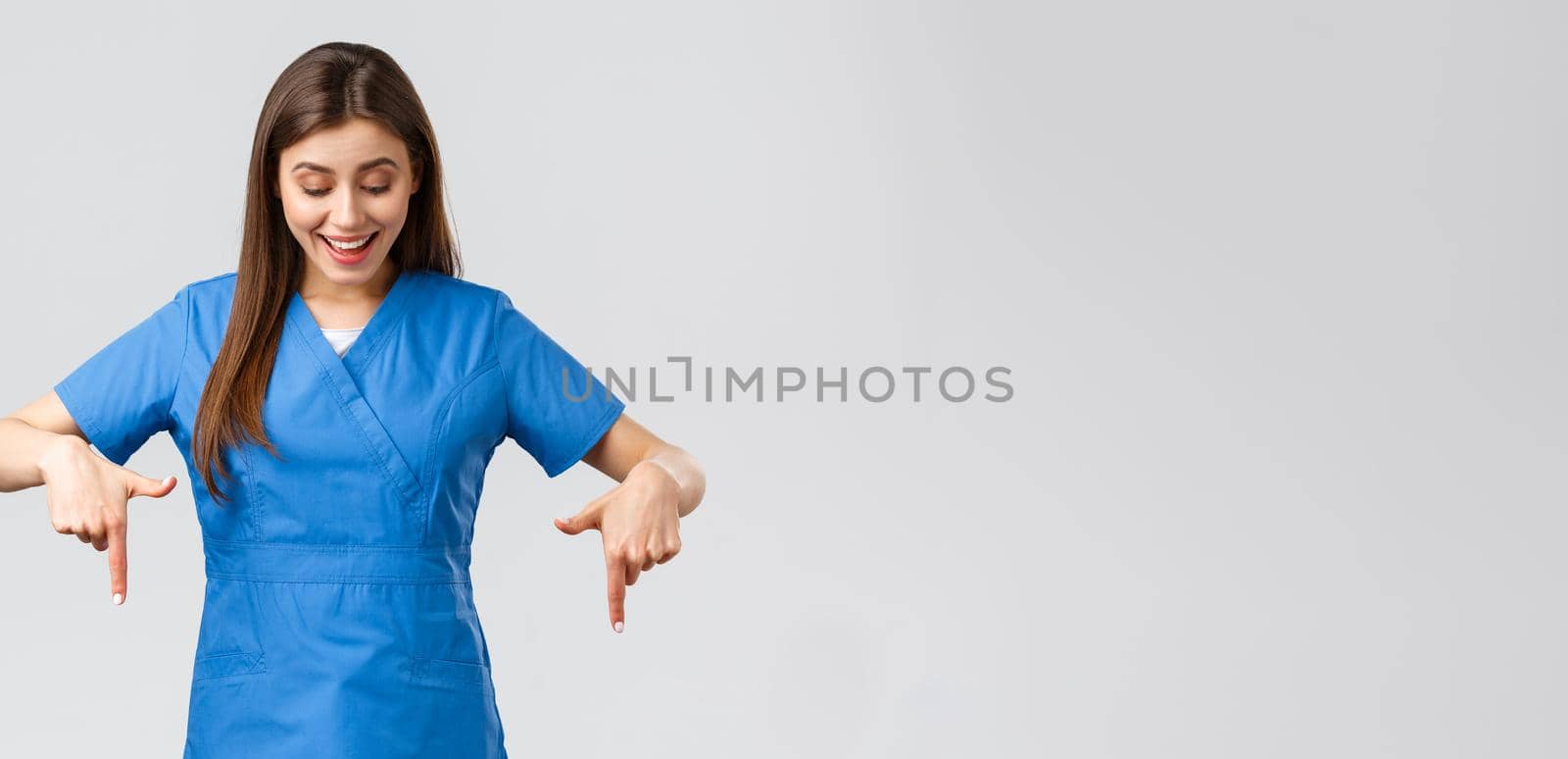 Healthcare workers, prevent virus, covid-19 test screening, medicine concept. Happy and excited pretty female nurse or doctor in blue scrubs, smiling as reading great news, pointing fingers down by Benzoix