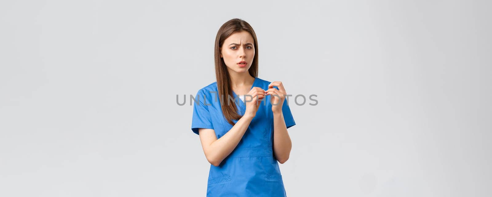 Healthcare workers, prevent virus, insurance and medicine concept. Skeptical or confused female doctor or nurse in blue scrubs, look at fingernails and turn head camera troubled, cant understand.