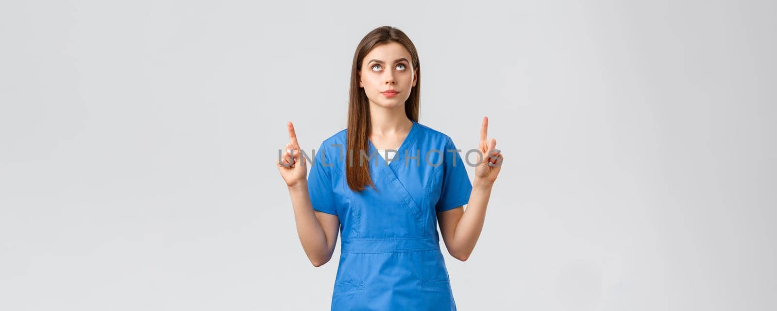 Healthcare workers, prevent virus, covid-19 test screening, medicine concept. Concerned, serious and focused female doctor or nurse in blue scrubs, pointing fingers and looking up at banner.