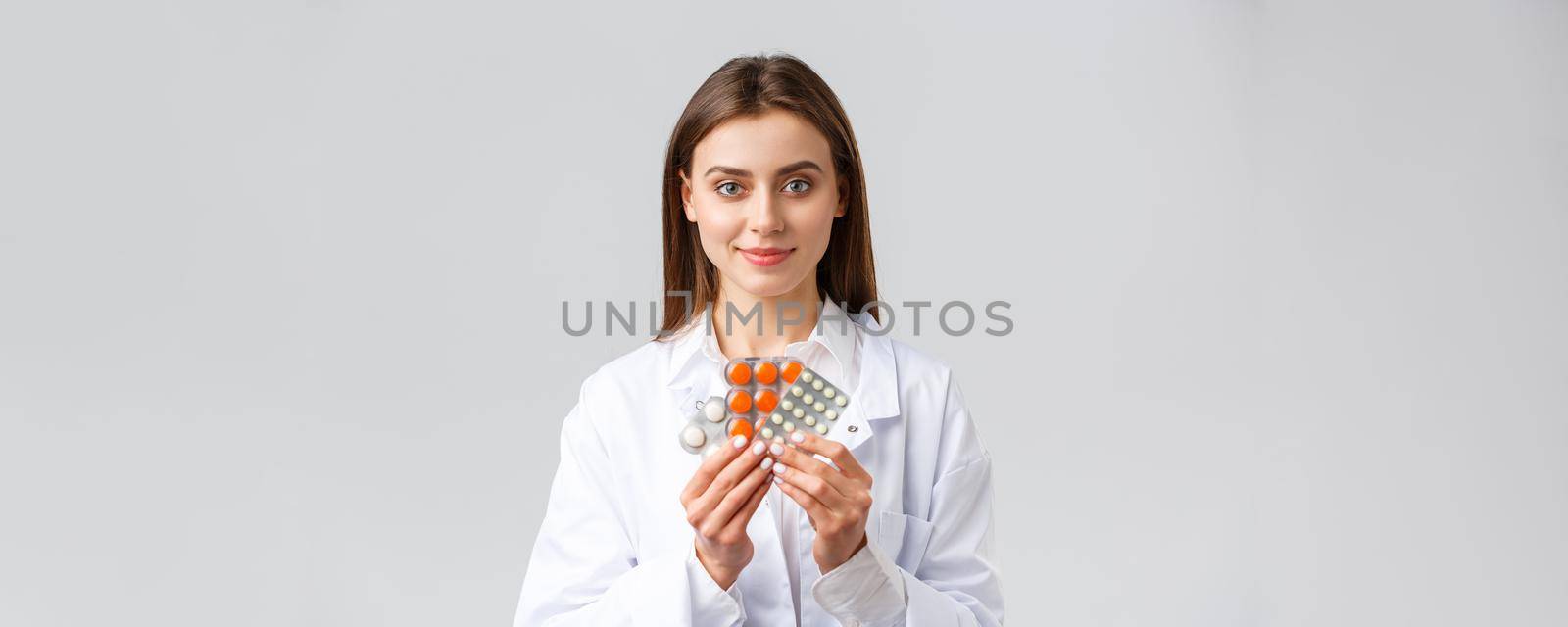 Covid-19, preventing virus, health, healthcare workers and quarantine concept. Physician in medical white scrubs, attractive female doctor showing medicine, different pills, smiling as recommend it by Benzoix