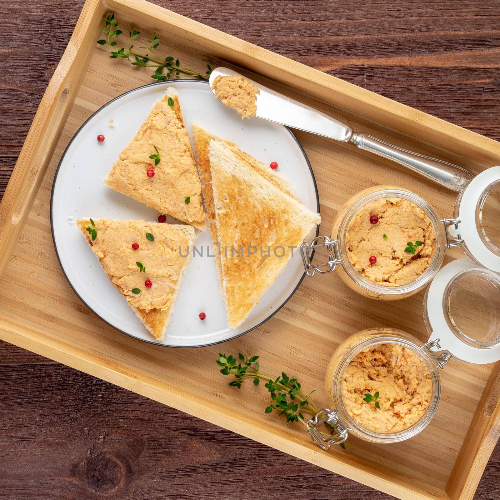 Fresh homemade chicken pate on a toasted bread on tray over rustic background, top view