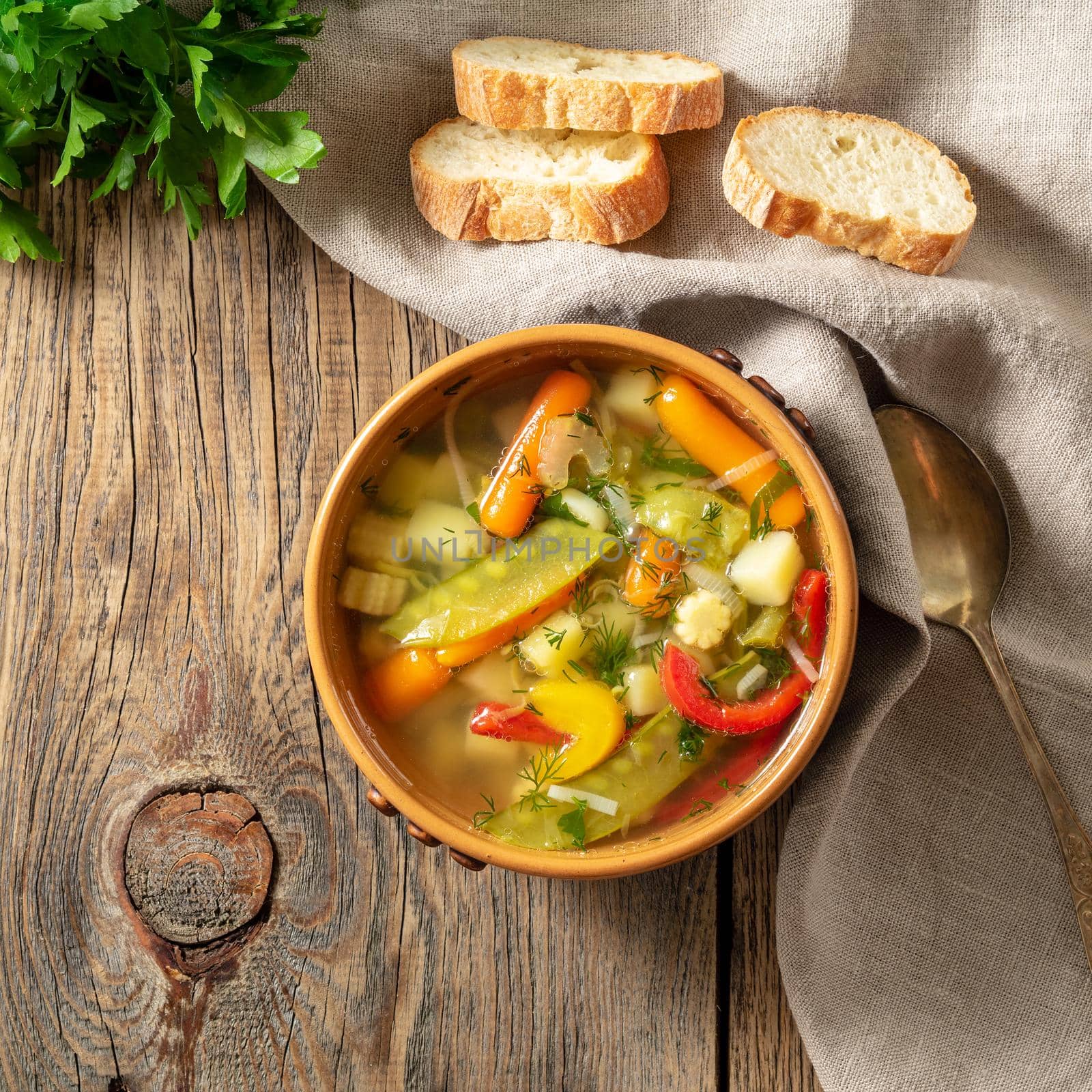 Bright spring vegetable dietary vegetarian soup. Top view, brown rustic wood background, linen napkin. by NataBene