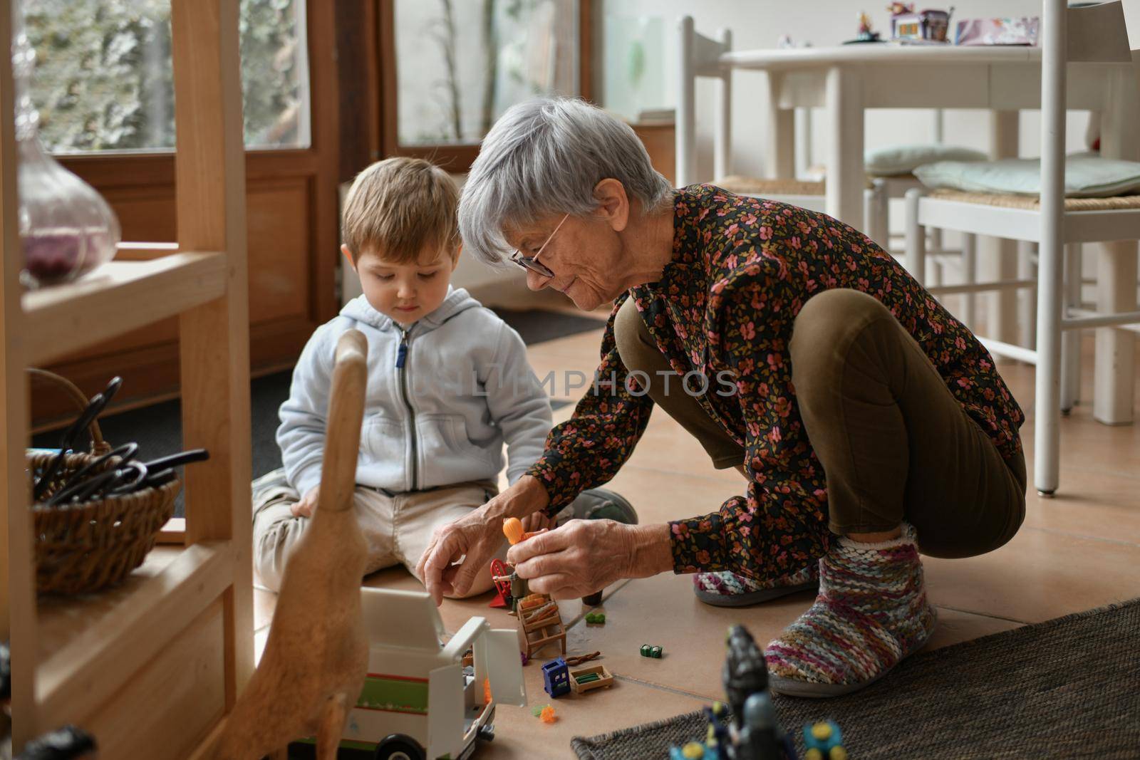 Gray-haired grandmother plays with her little grandchildren in a house