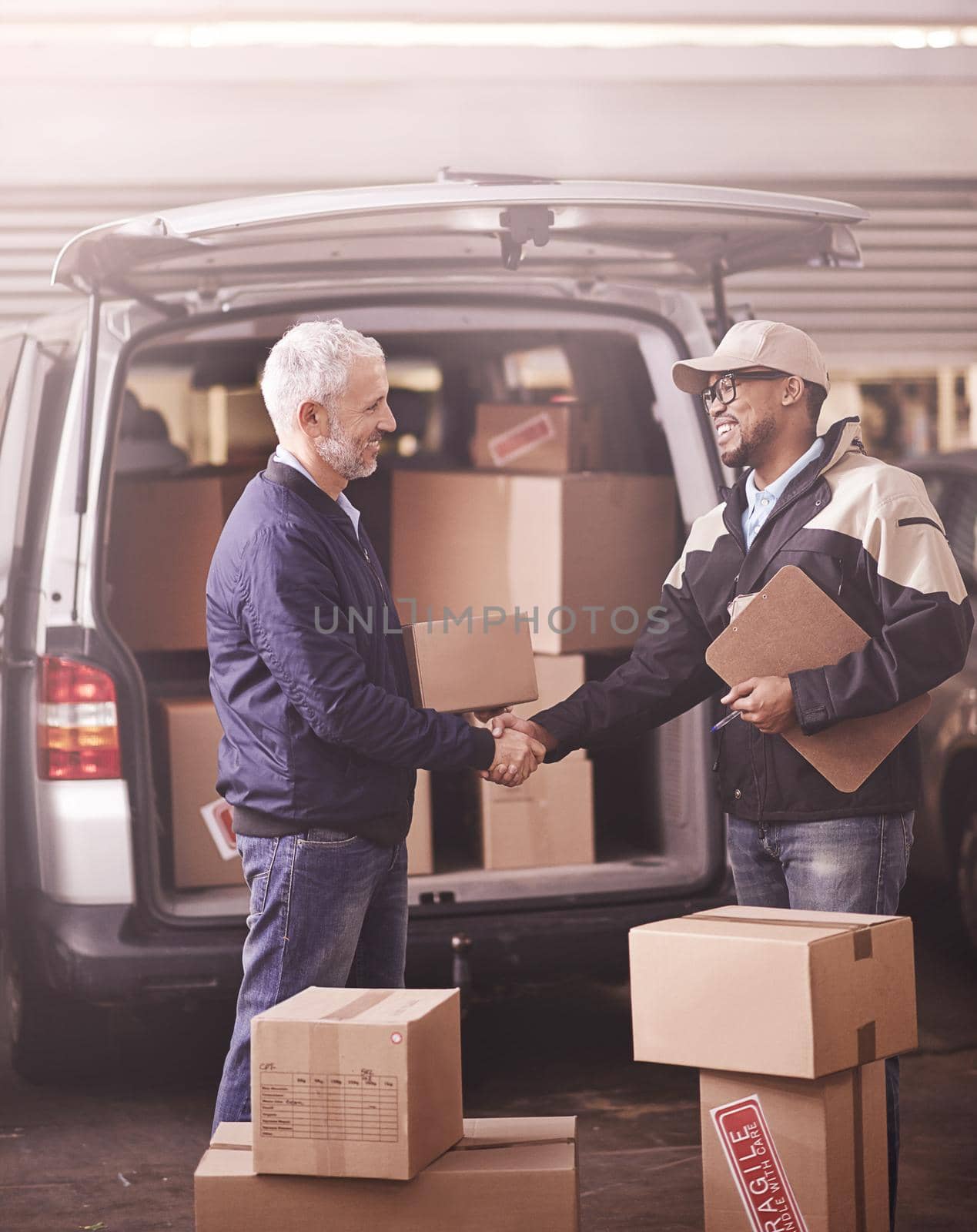 Shot of two delivery men shaking hands next to a van filled with boxes.