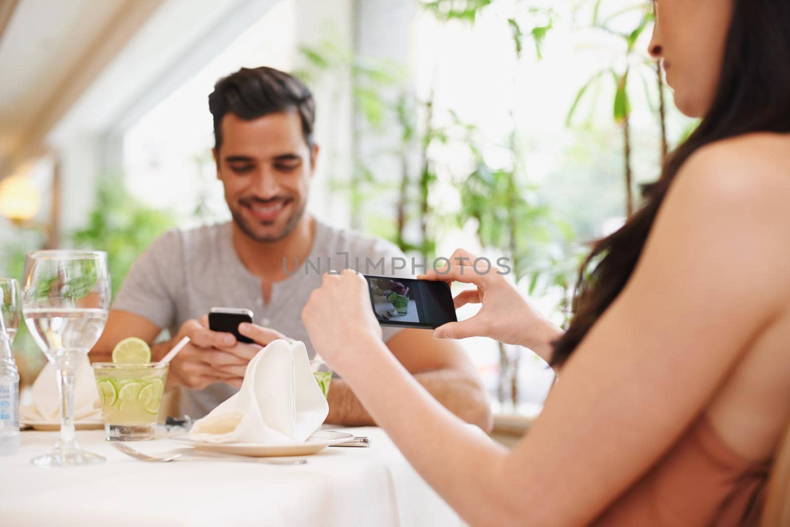 Romantic memories. A woman taking a picture while dining out with her partner at a restaurant. by YuriArcurs