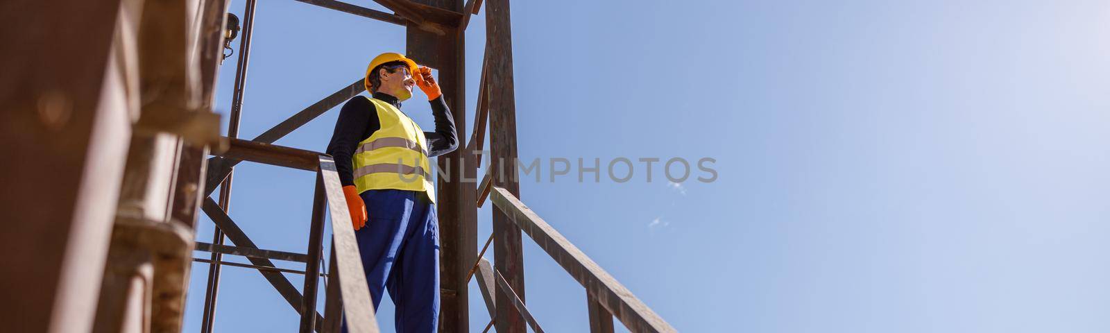 Full length of man factory engineer standing on top of staircase and looking at sky