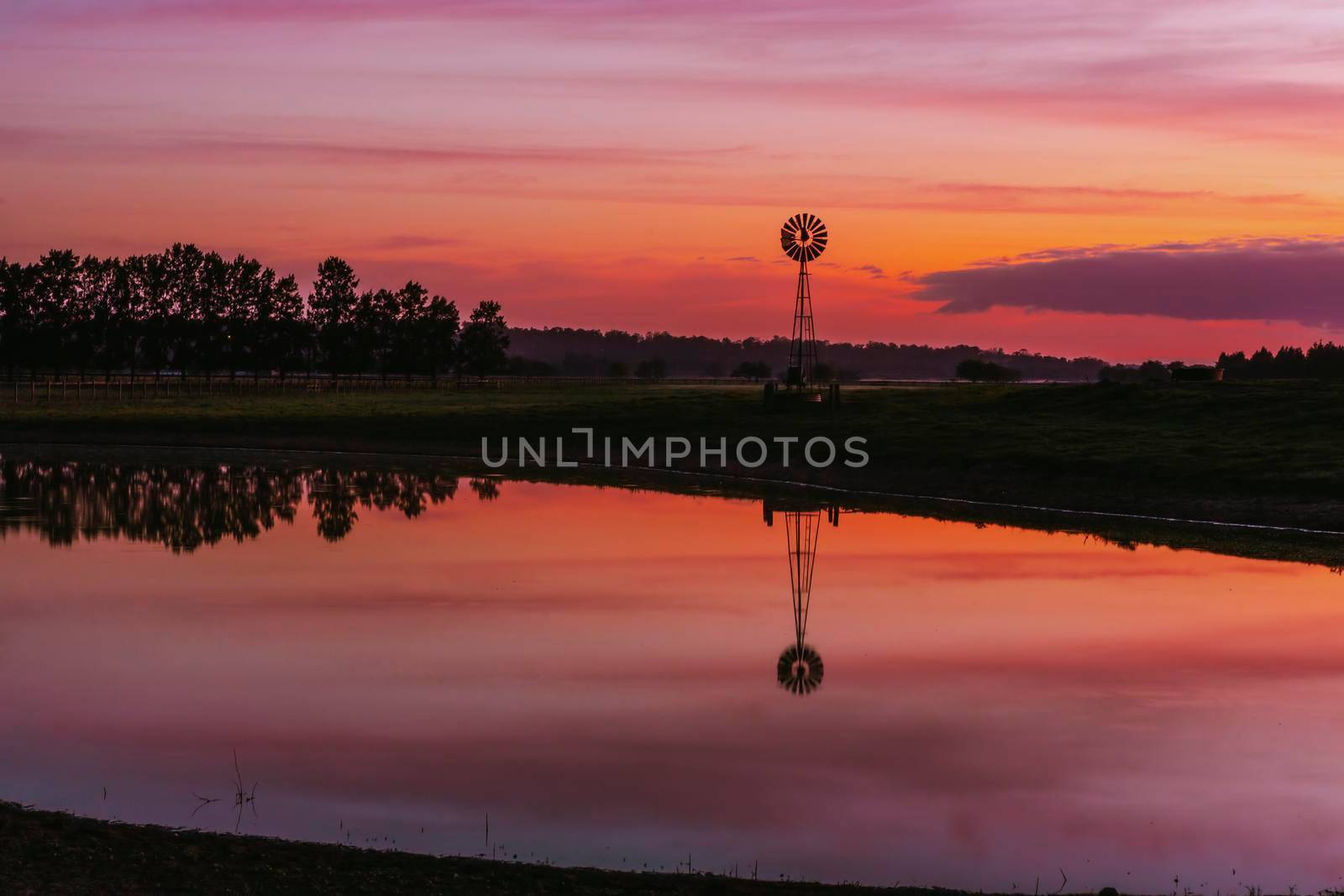 Old farm windmill in a rural field with vivid sunrise sky by lovleah