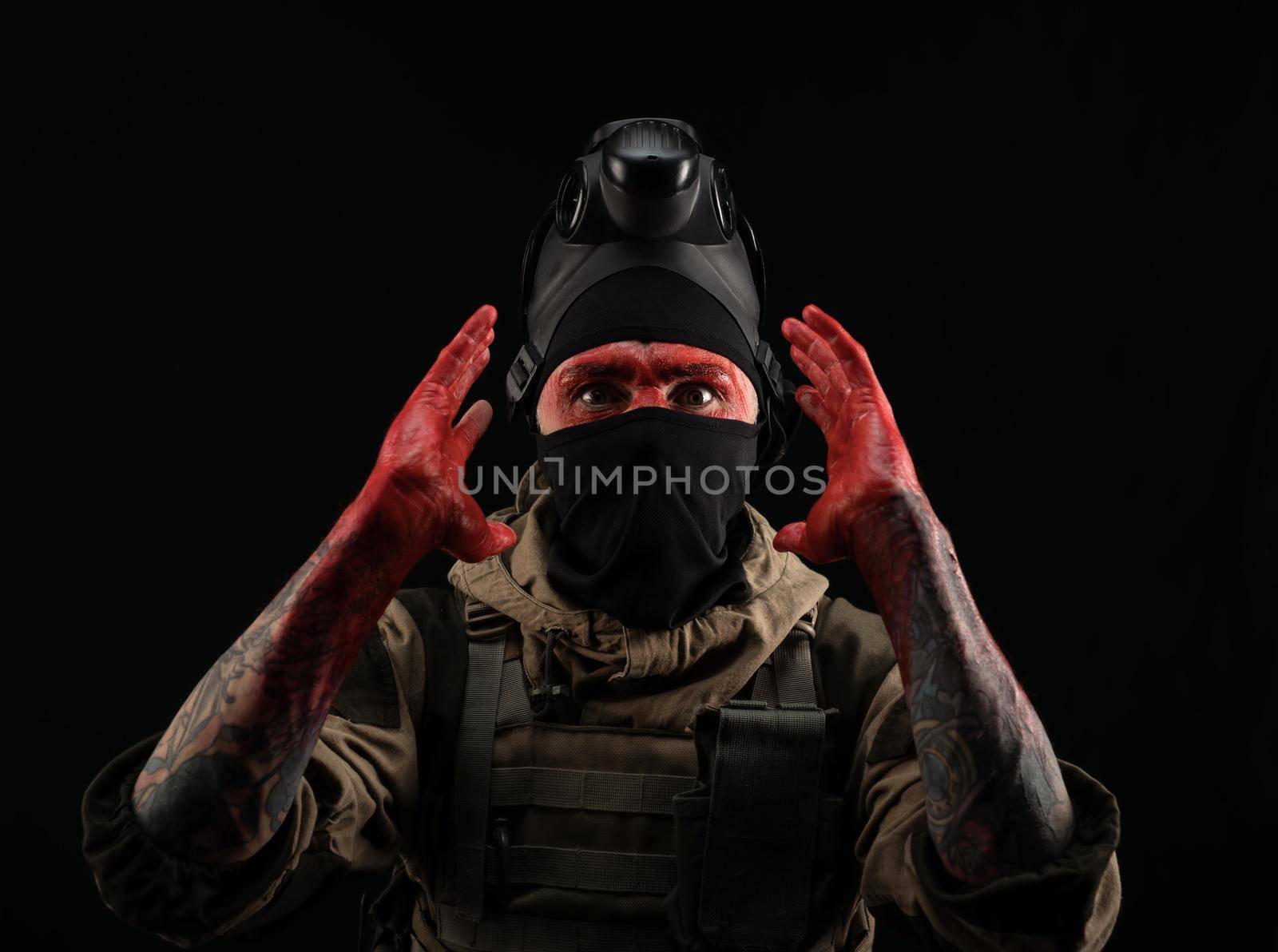 the photo of a man in a military uniform and balaclava with a bloody face and hands up to the elbow in blood on a black background