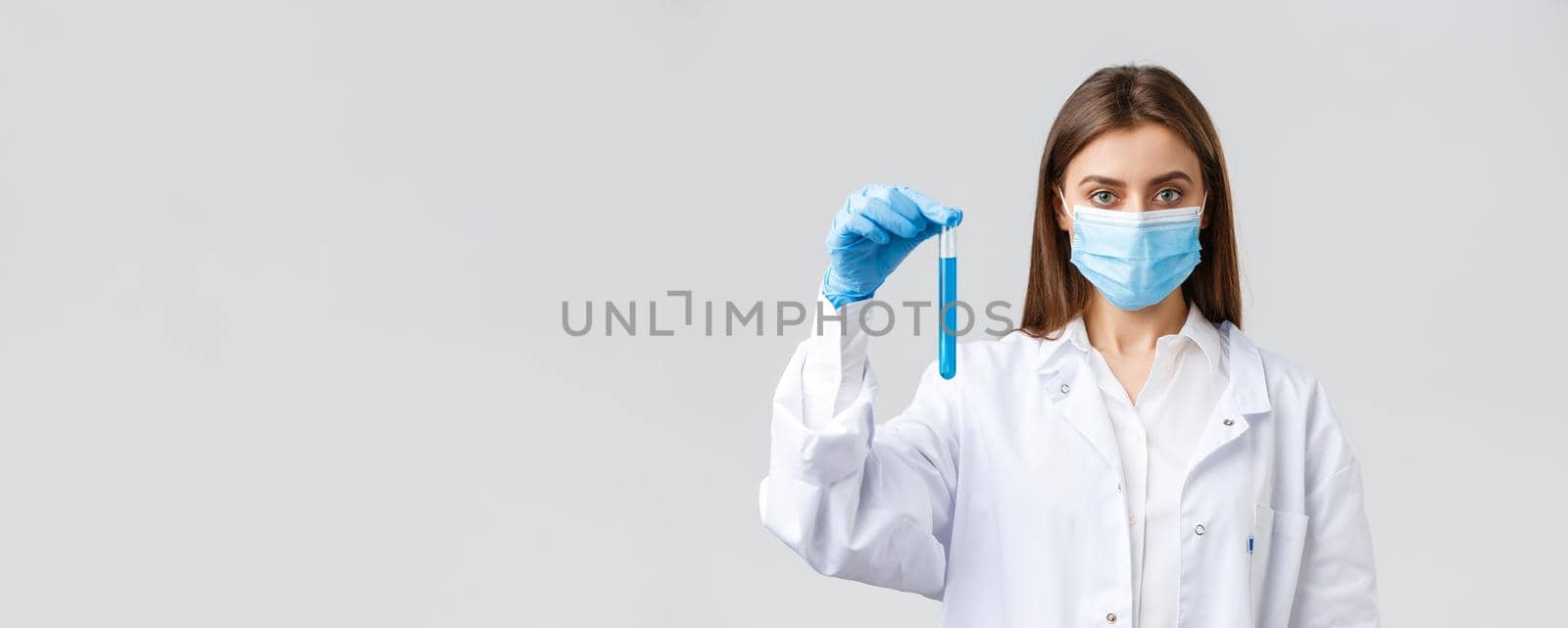 Covid-19, preventing virus, healthcare workers and quarantine concept. Determined female doctor or nurse in medical mask and scrubs, showing test-tube with coronavirus vaccine by Benzoix