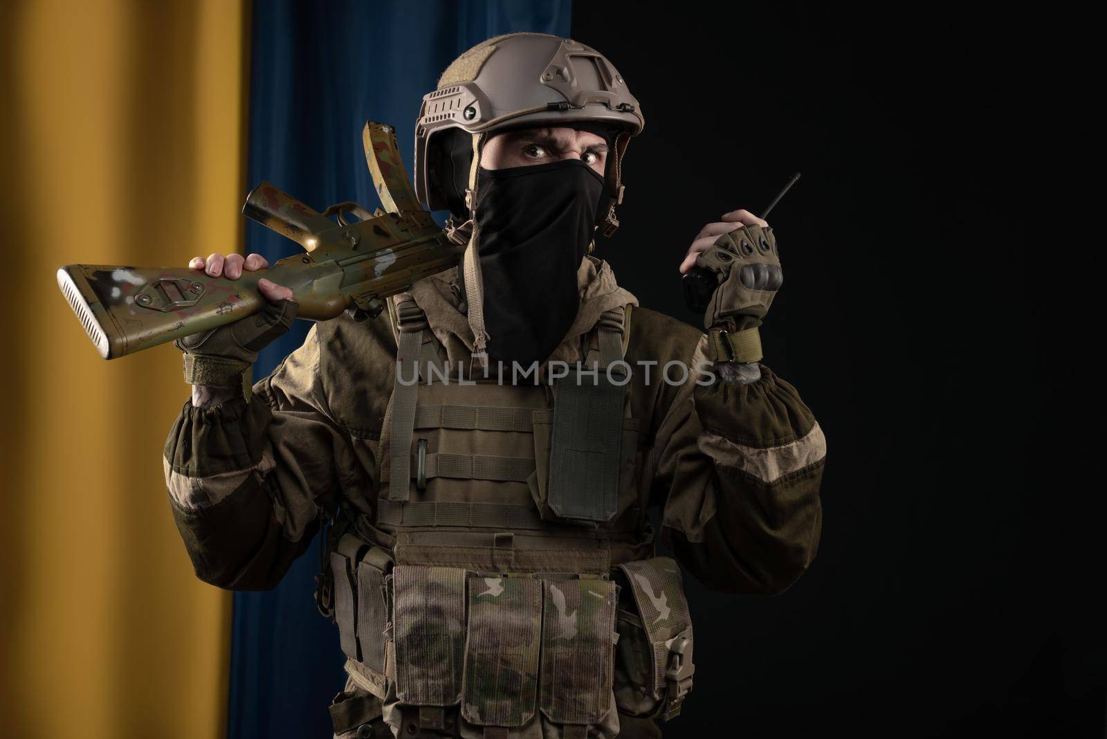 male soldier in a military uniform and helmet with a weapon on the background of the national flag of Ukraine