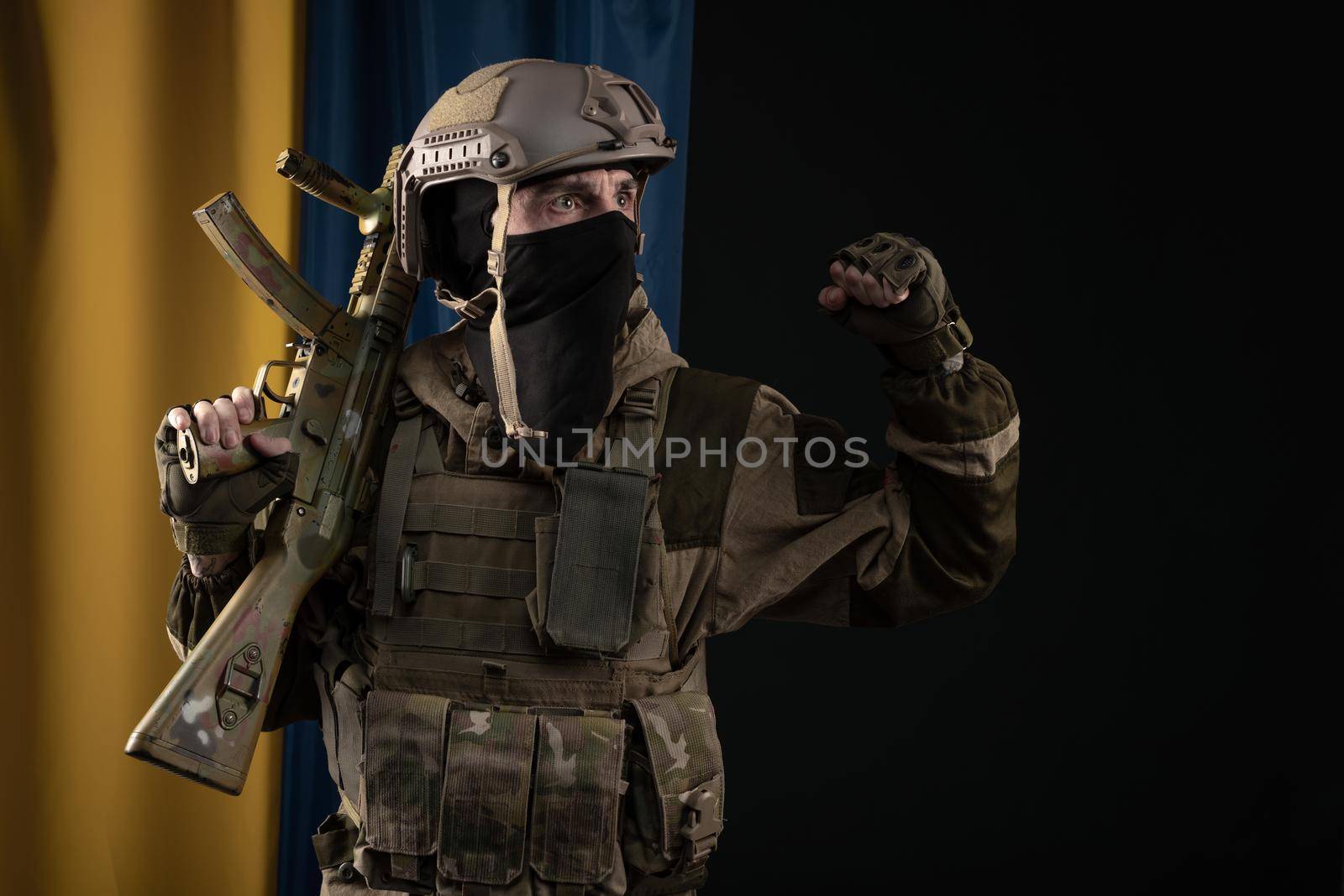 male soldier in a military uniform and helmet with a weapon on the background of the national flag of Ukraine