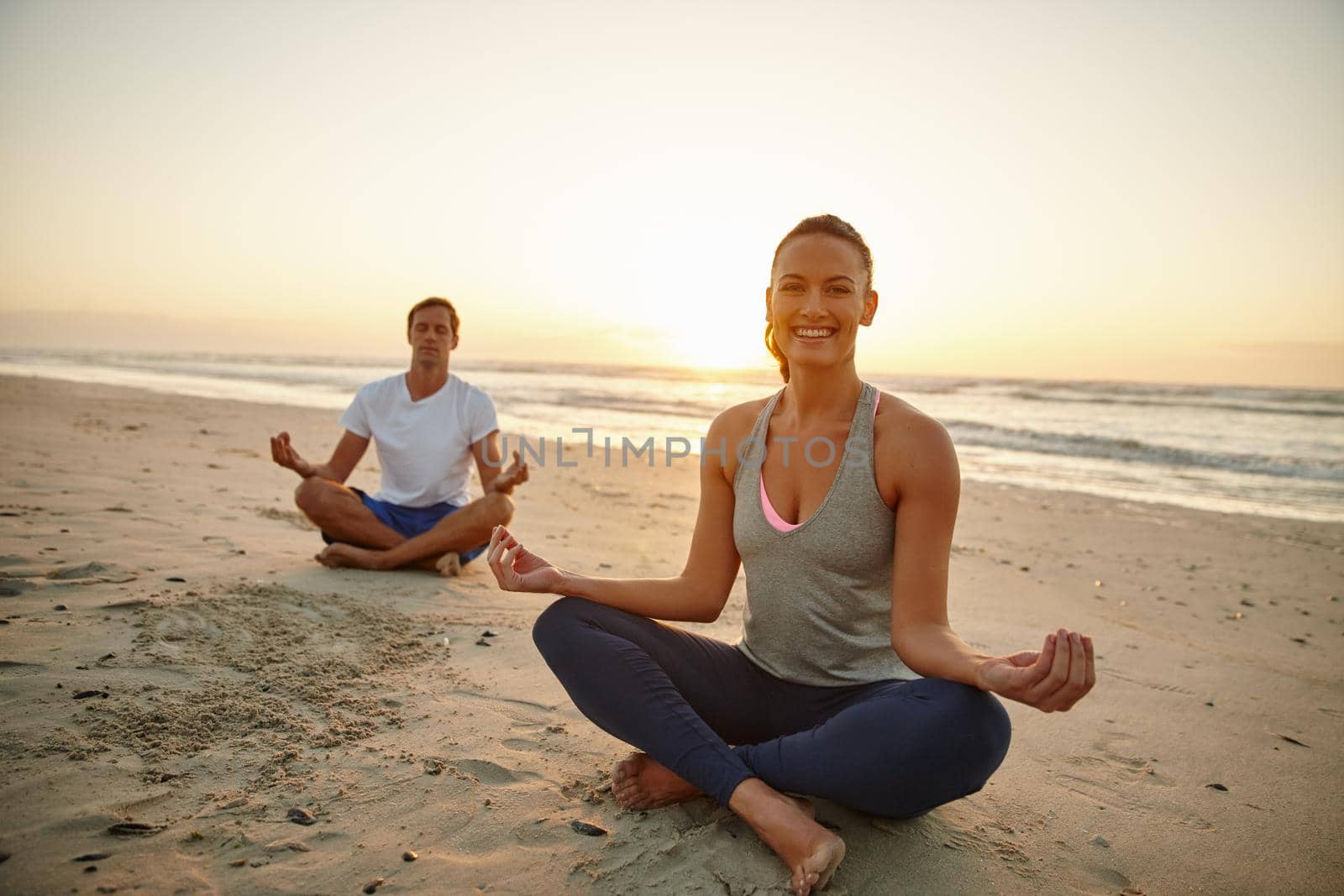 Portrait of a couple doing yoga on the beach at sunset.