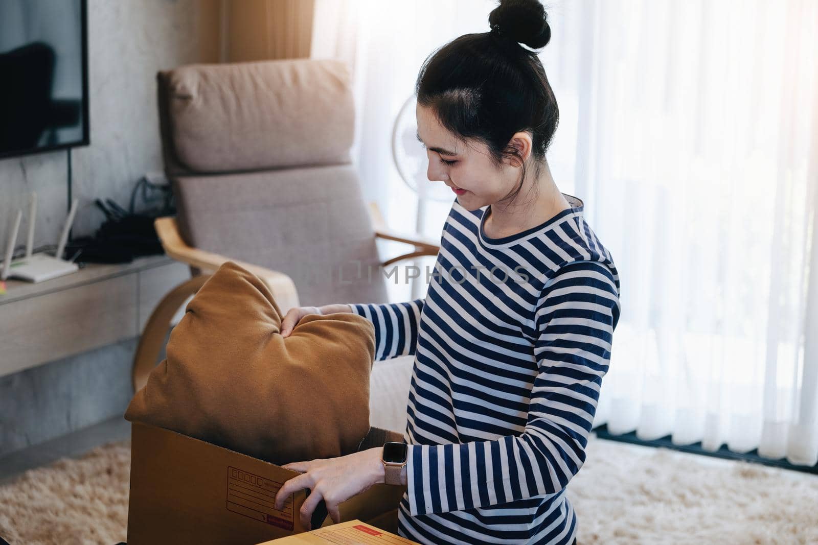 Online merchandising business idea, a beautiful girl is packing pillows in a shipping box to prepare to send items to customers according to orders received from customers. by Manastrong