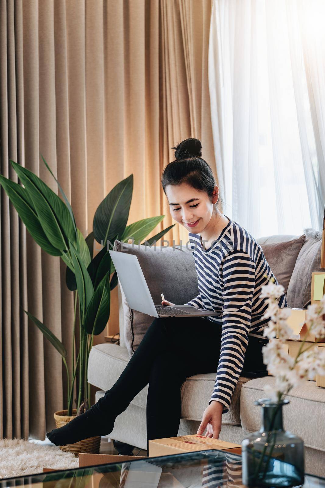 Online merchandising business idea, a beautiful girl is using a computer to check orders to deliver parcels to customers according to orders received from customers. by Manastrong