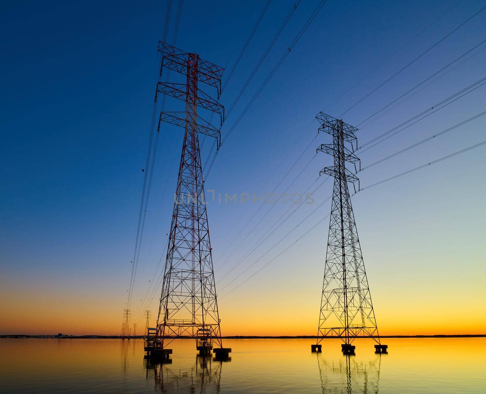 High voltage transmission lines crossing Wheeler Lake at dusk near Athens AL. Electricity pylons at sunset. Power and energy.