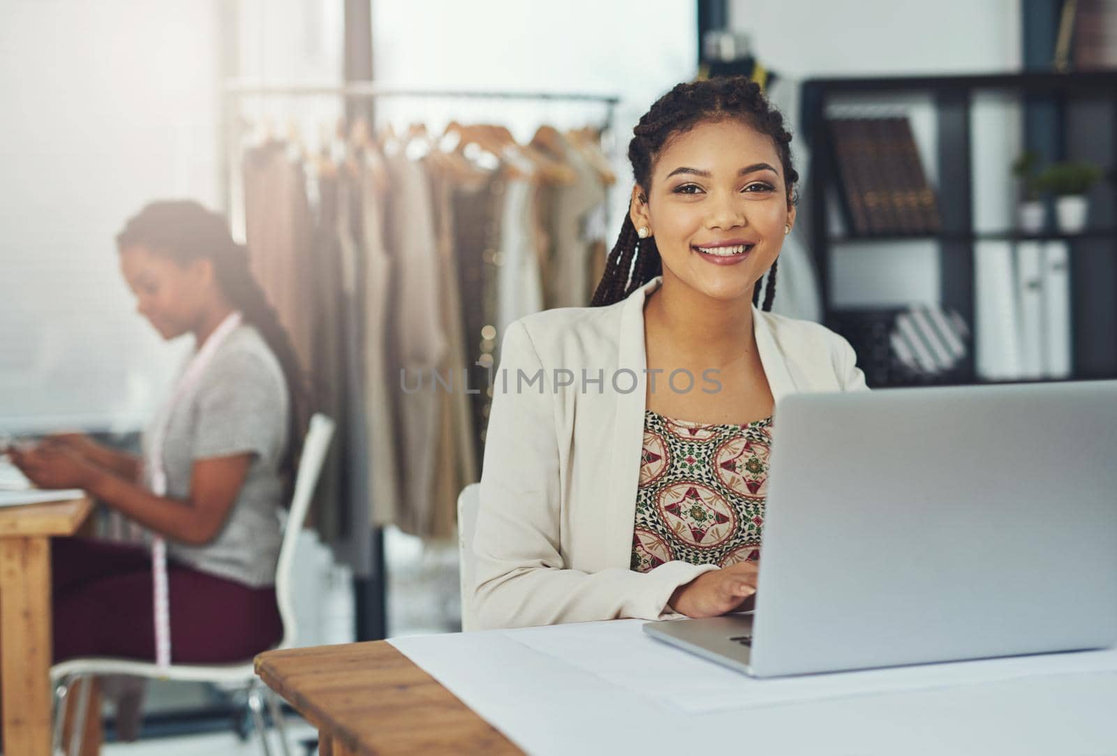 Shot of a fashion designer working on her laptop with her colleague blurred out.