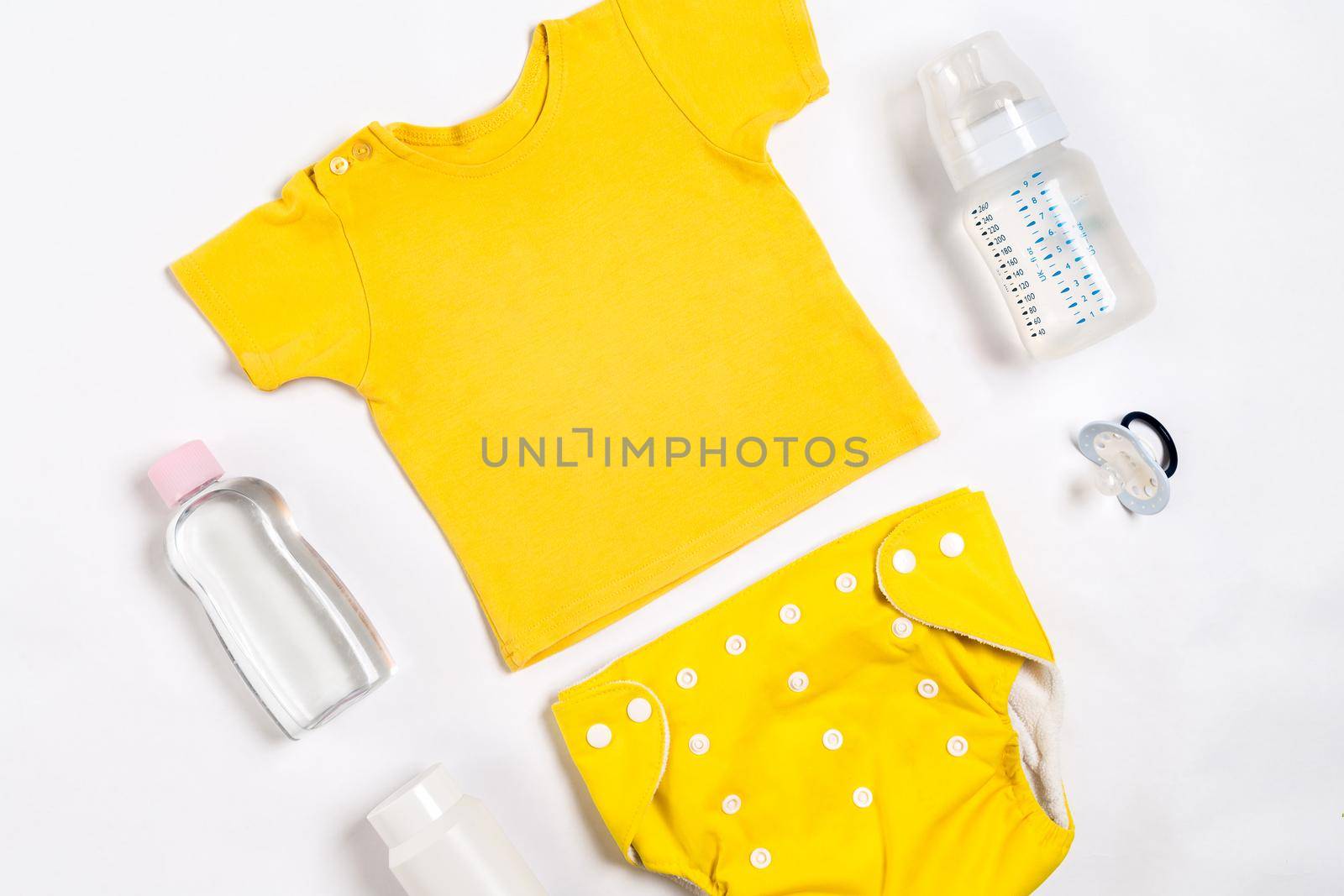 Yellow children's costume, bottle and orthodontic pacifier on a white background. Top view. Copy space. Flat lay. Still life
