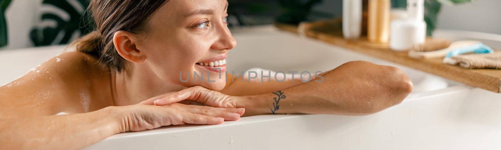 Portrait of happy young woman smiling aside while resting in bathtub at luxury spa resort. Wellness, beauty and care concept