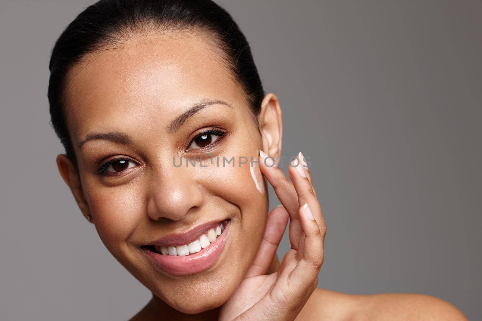 Cropped shot of a beautiful young woman applying face cream while standing in a studio.