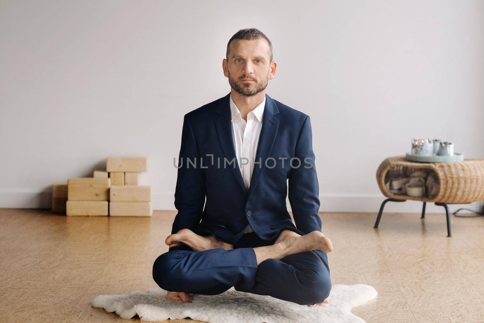 A man in a strict suit does Yoga while sitting in a fitness room.