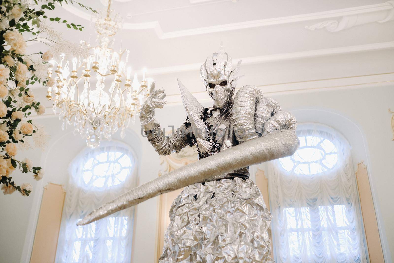 A man in a silver suit and a mask on stilts in the interior of the castle.