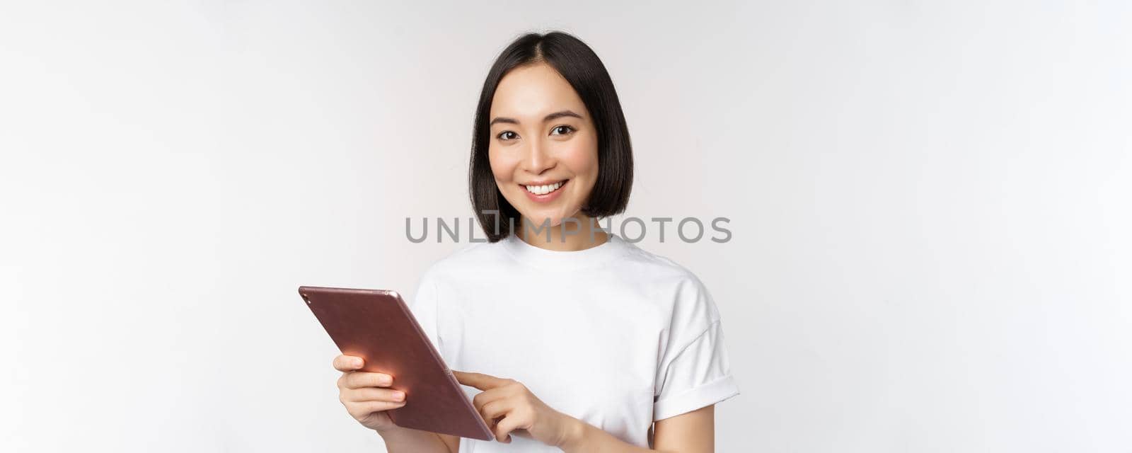 Asian girl using digital tablet, working with gadget, shopping online, standing over white background.