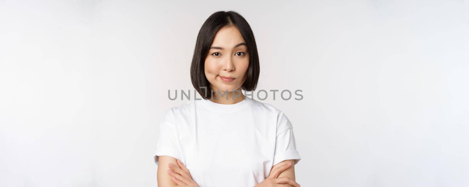 Close up of korean girl, looking skeptical, cross arms on chest and smirk, stare with disbelief at camera, standing over white background by Benzoix