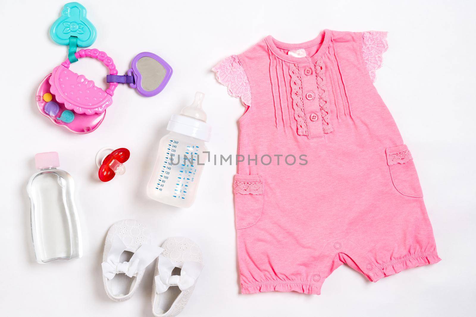 Pink children's costume, bottle and orthodontic pacifier on a white background. Top view. Copy space. Flat lay. Still life