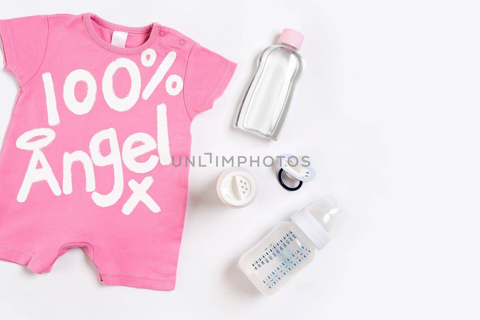 Pink children's costume, bottle and orthodontic pacifier on a white background. Top view. Copy space. Flat lay. Still life