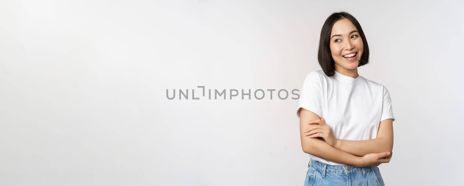 Portrait of happy asian woman smiling, posing confident, cross arms on chest, standing against studio background.