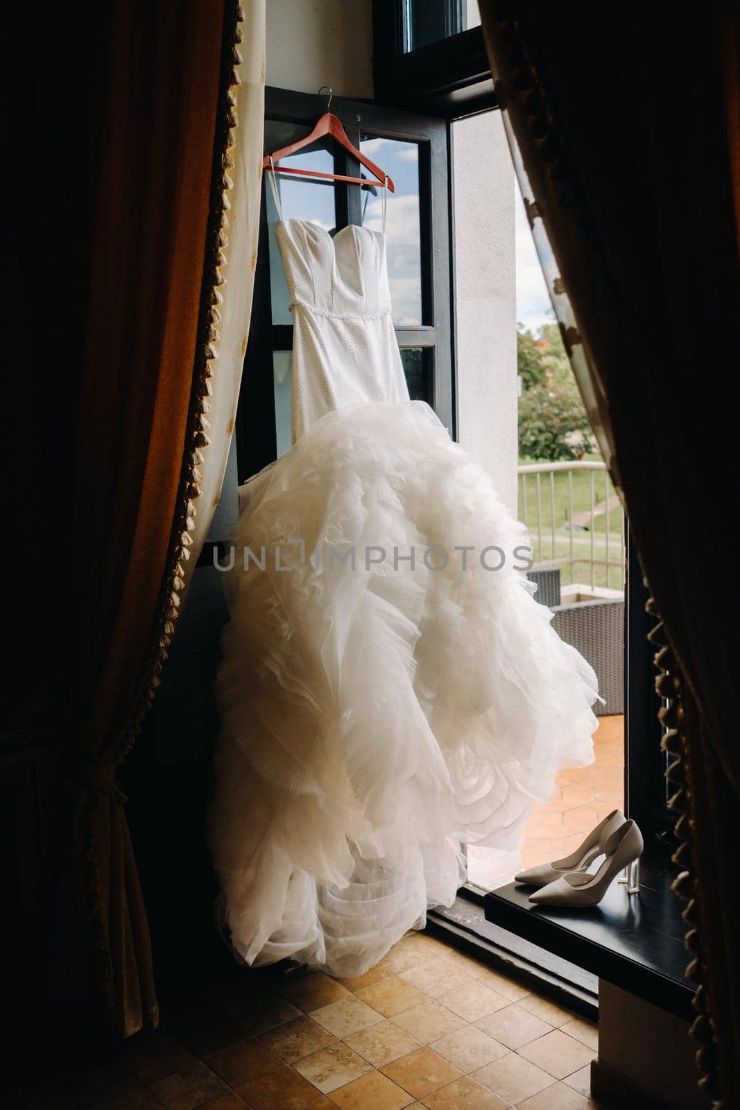 a white wedding dress hangs on a hanger near the window.