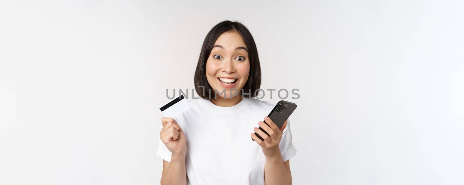 Online shopping. Happy asian woman using credit card and smartphone app, paying on website via mobile phone, white background by Benzoix