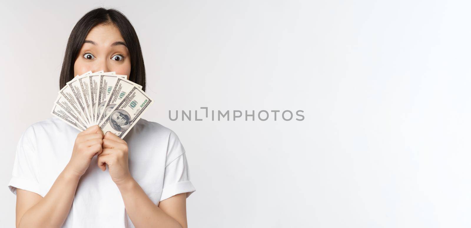 Happy asian girl holding money, cash near face, concept of microcredit and finance, white studio background. Copy space