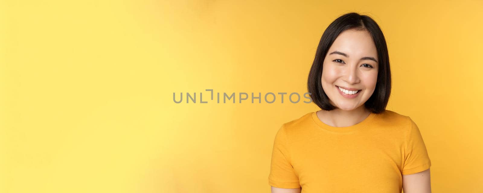 Close up portrait of beautiful asian woman smiling, looking cute and tender, standing against yellow background by Benzoix