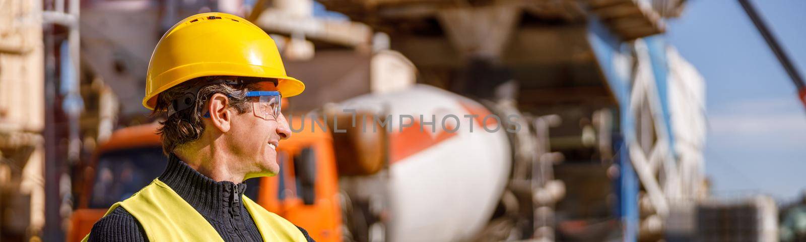 Cheerful man factory worker wearing safety helmet and work vest while keeping arms crossed and smiling