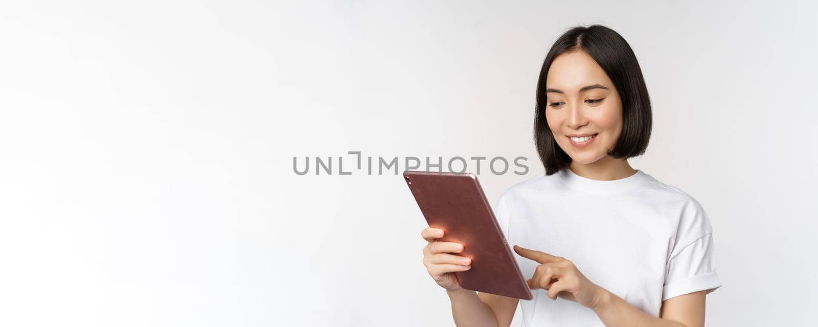 Asian girl using digital tablet, working with gadget, shopping online, standing over white background.