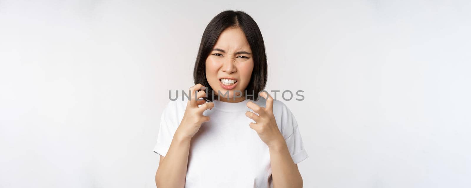 Angry asian woman cursing, looking outraged and annoyed, clench teeth and frowning furious, standing over white background by Benzoix