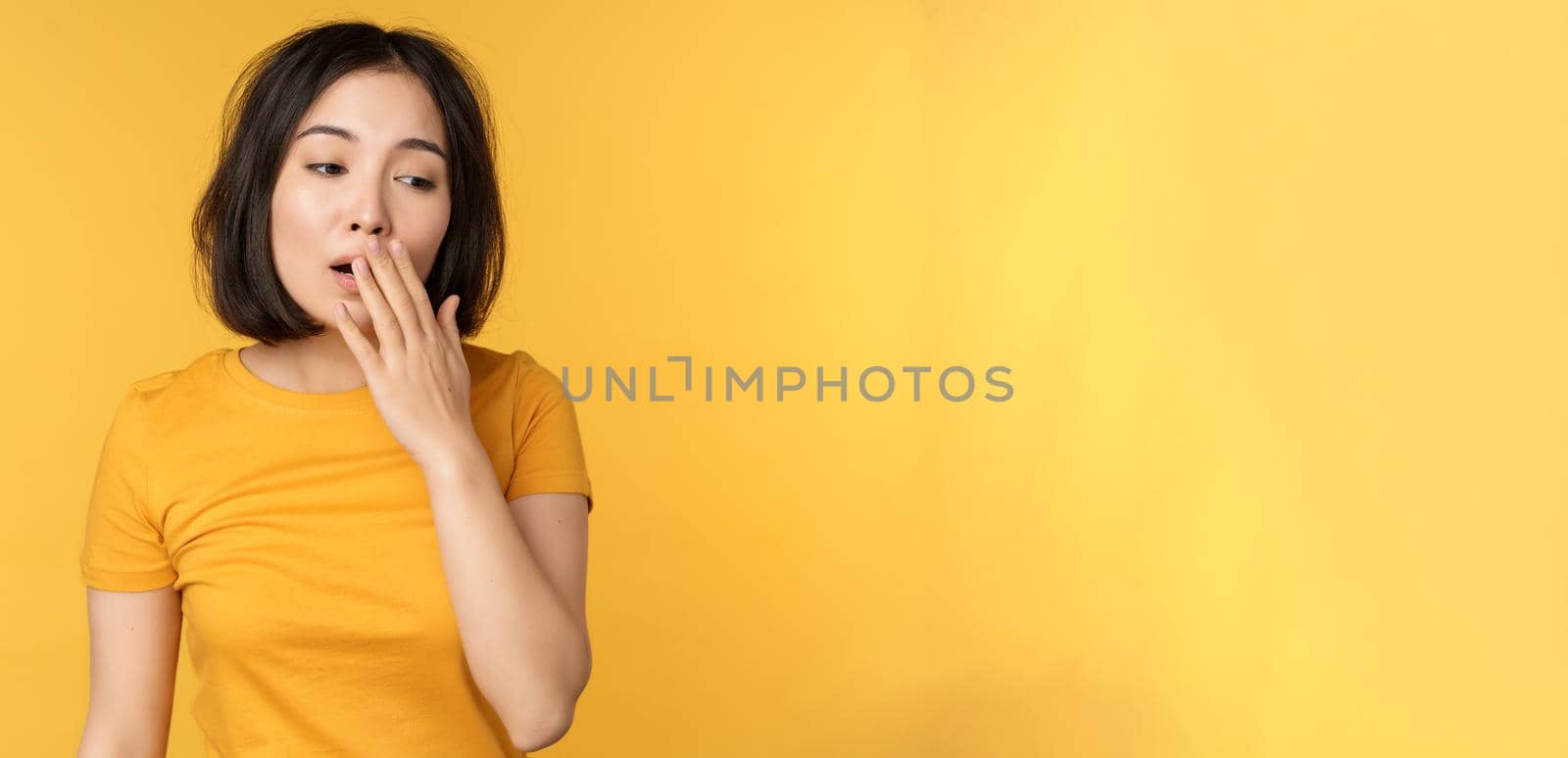 Image of young asian girl student, yawning, feeling tired, standing sleepy agaisnt yellow background by Benzoix