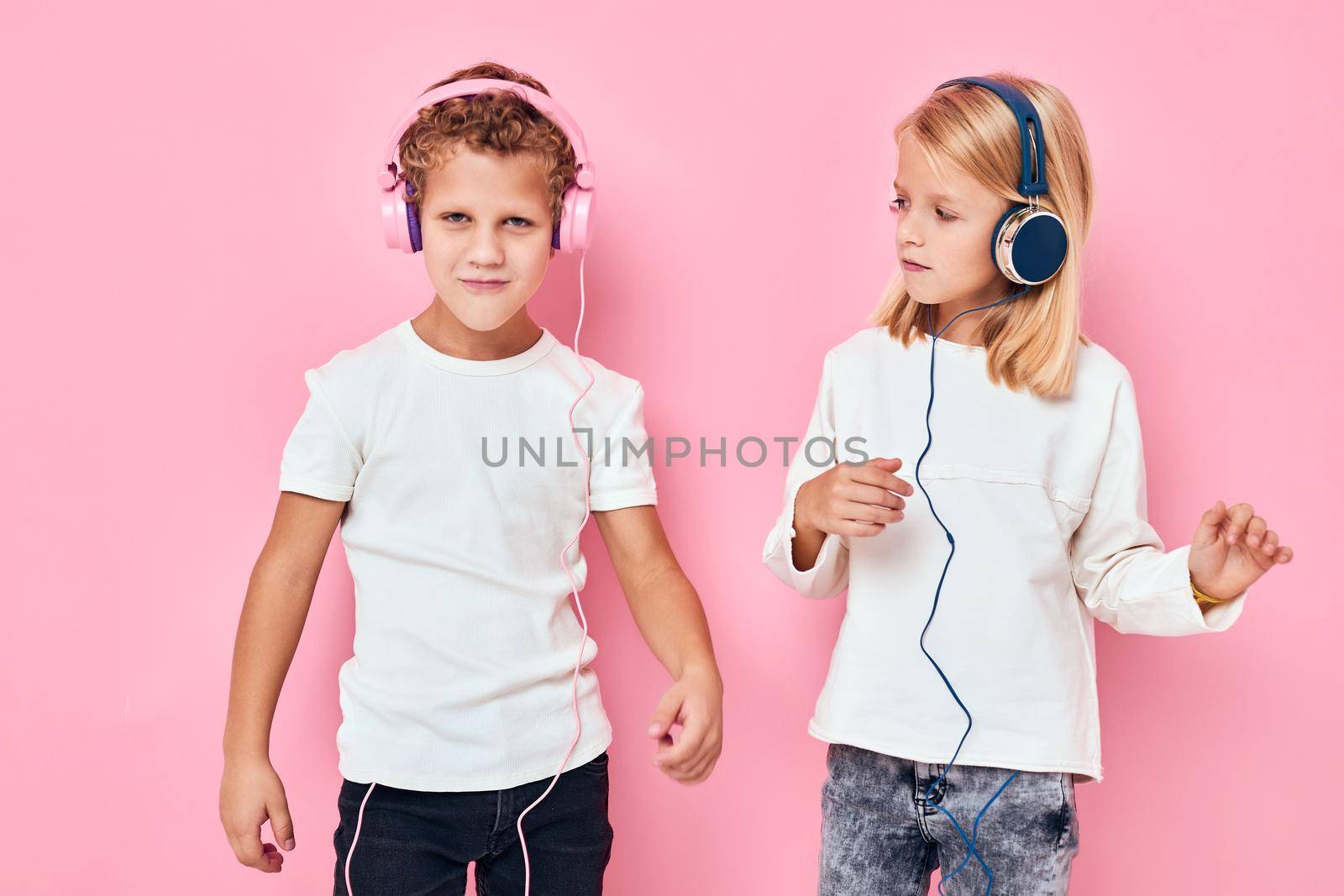 Stylish little boy and cute girl stand next to in headphones pink color background. High quality photo