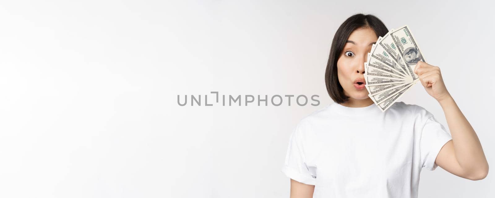 Happy asian girl holding money, cash near face, concept of microcredit and finance, white studio background. Copy space