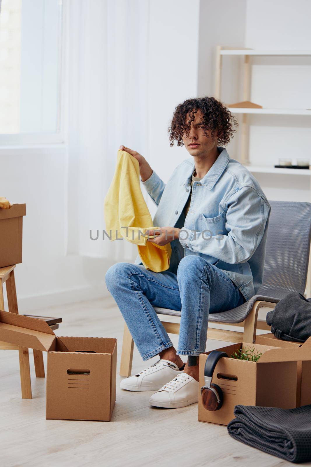 A young man cardboard boxes in the room unpacking interior by SHOTPRIME