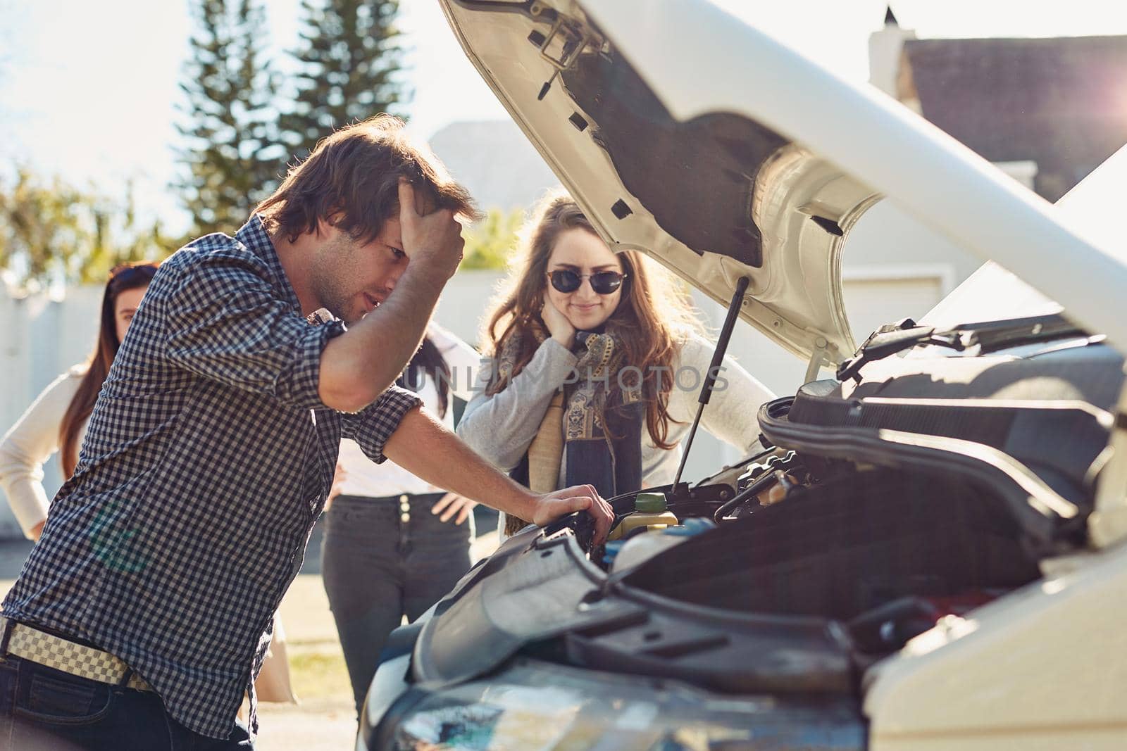 Shot of a young man looking under the hood of a broken down car.