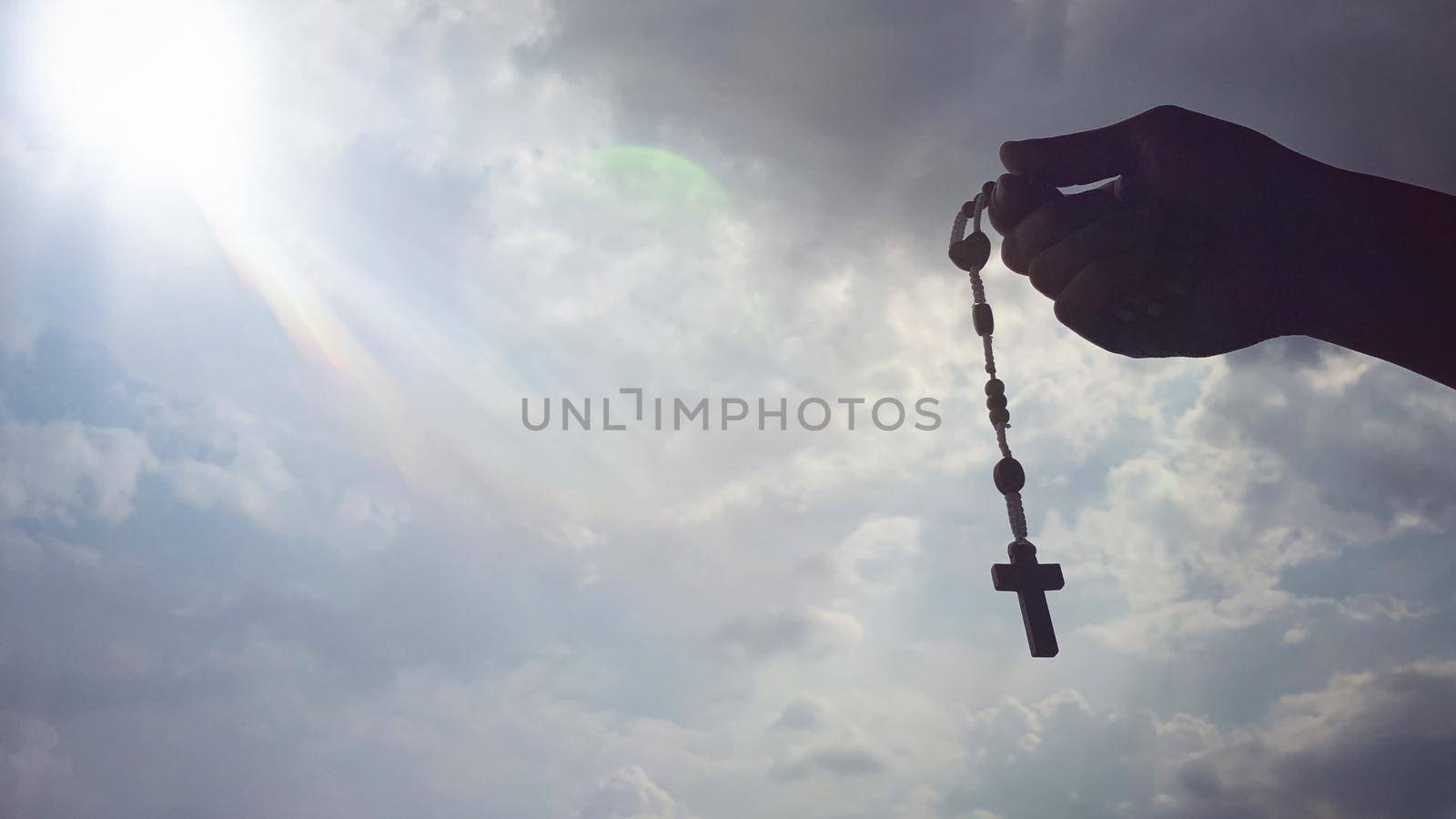 Christianity concept - hand holding Rosary with sky background. Religious