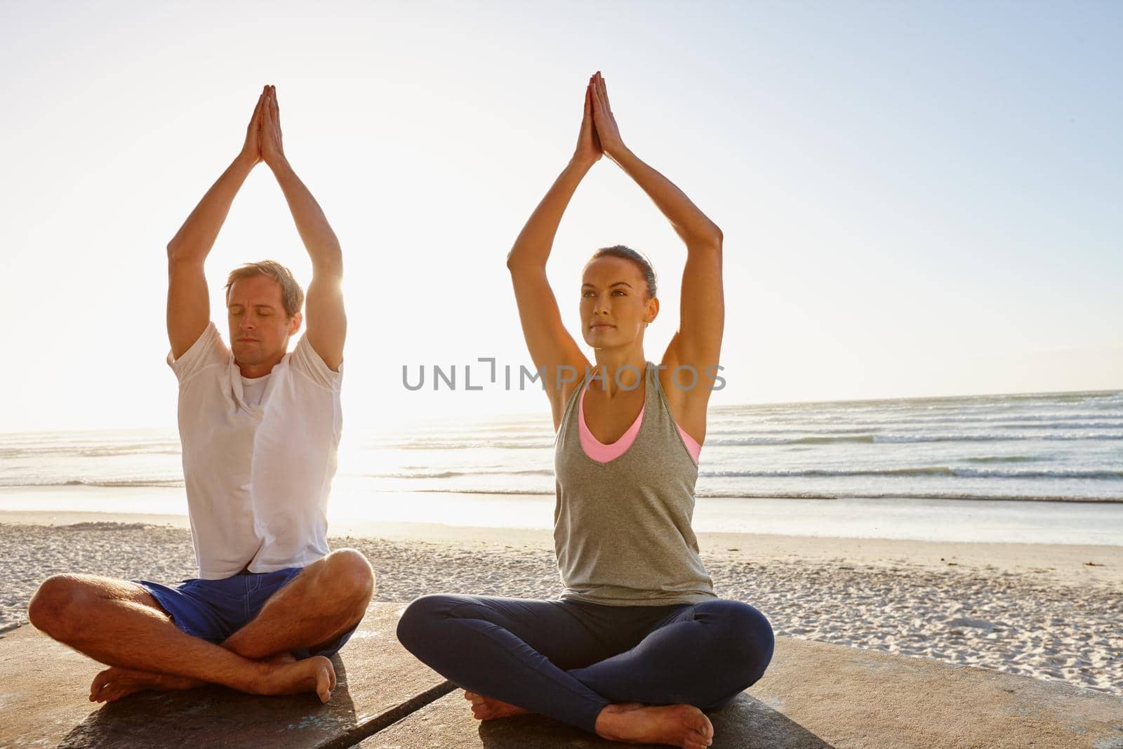Shot of a couple doing yoga at the beach at sunset.