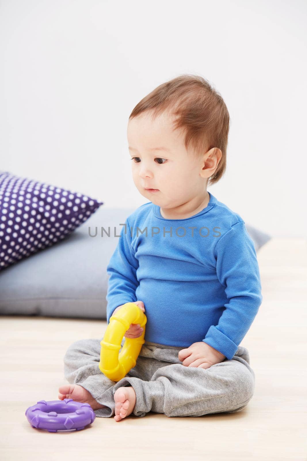 Hes a playful little guy.... Shot of a cute baby boy sitting on the floor and playing with his toys. by YuriArcurs
