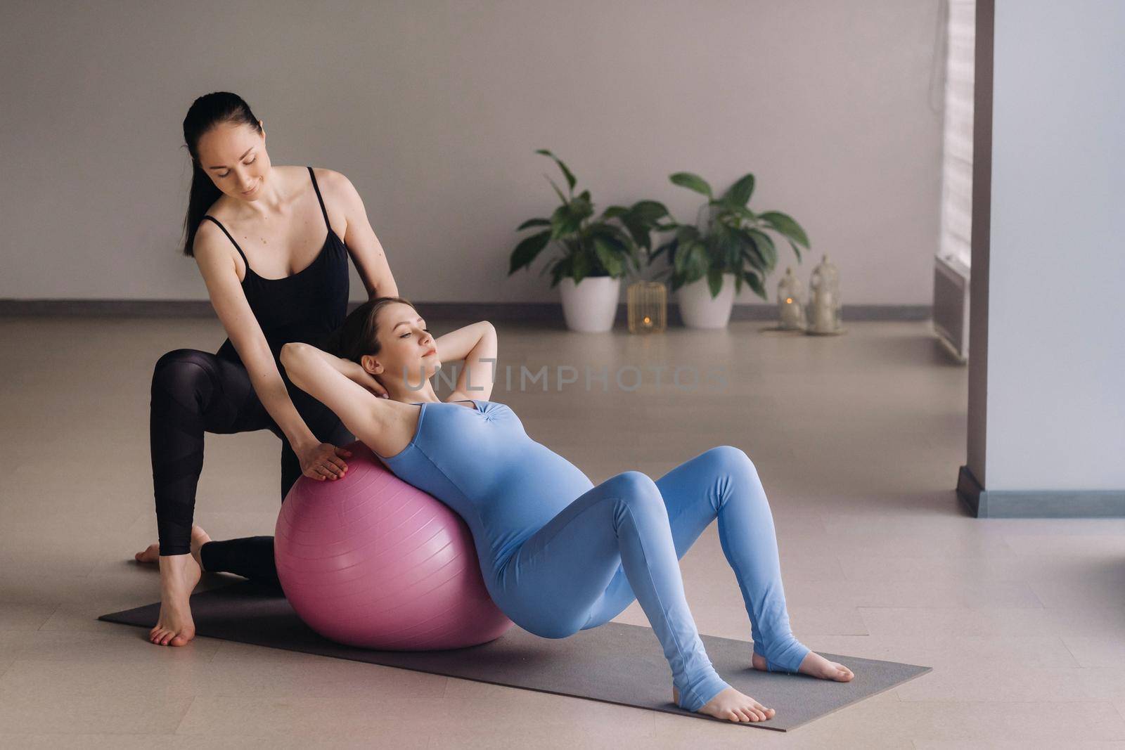 Pregnant woman with a trainer during fitness classes with a ball.