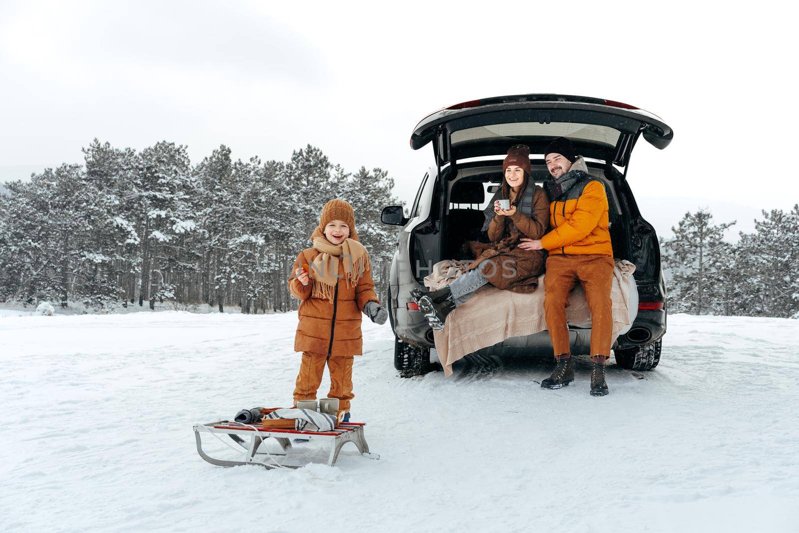 Winter portrait of a family sit on car trunk enjoy their vacation in forest by Fabrikasimf