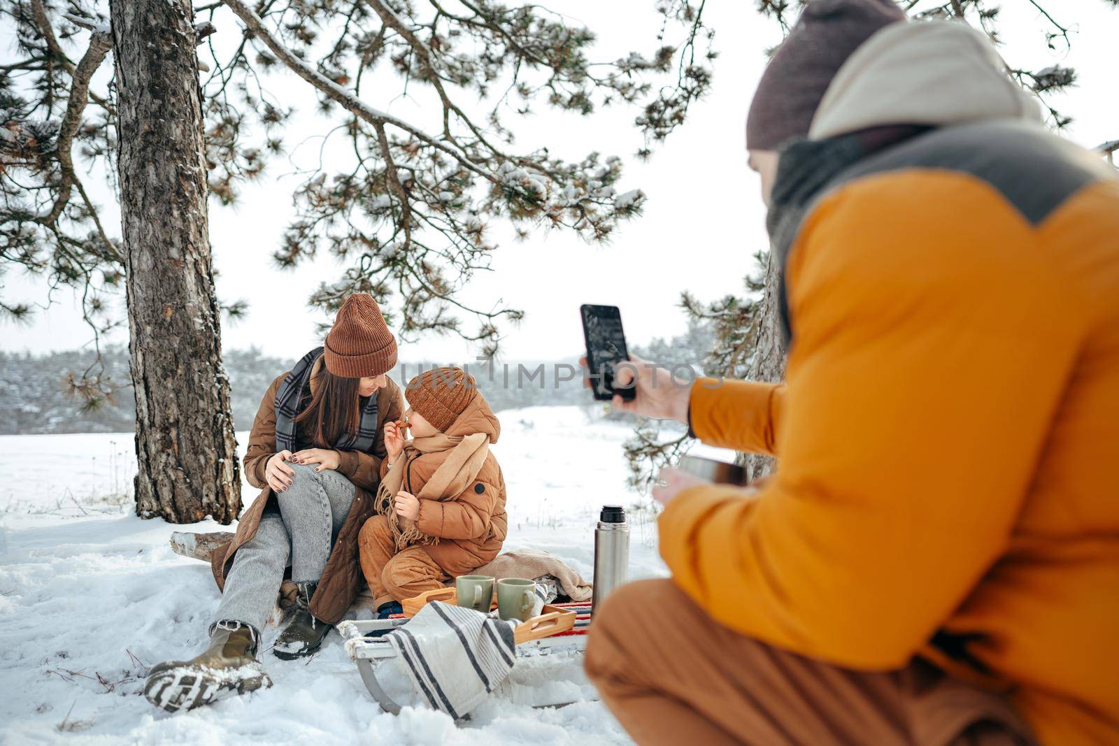 Happy family with cups of hot tea spending time together in winter forest, close up