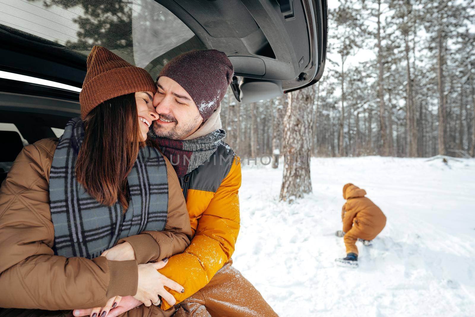 Lovely smiling couple sitting in car trunk in winter forest, close up