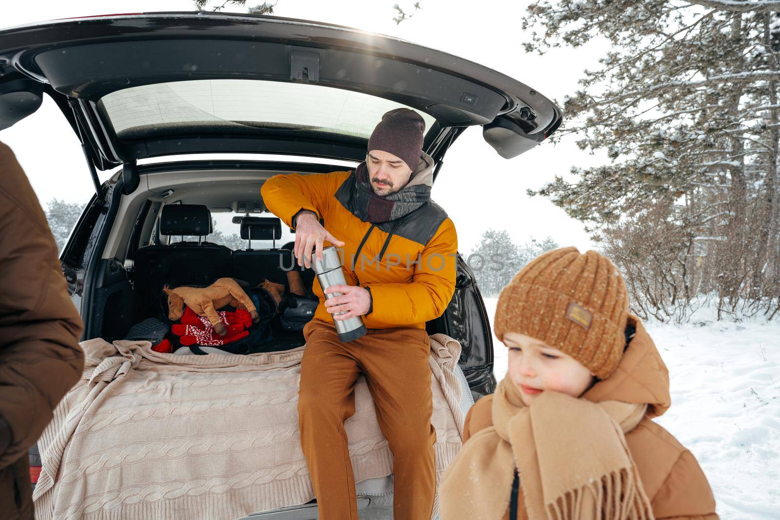 Winter portrait of a family sit on car trunk enjoy their vacation in forest by Fabrikasimf